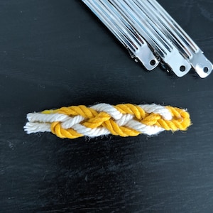 Könnte beinhalten: Drei silberne Haarklammern und ein geflochtenes Haarband aus gelbem und weißem Seil.