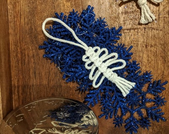 Pode incluir: Ornamento de macramé branco com uma borla pendurada em um floco de neve azul brilhante.