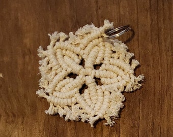 Pode incluir: Um chaveiro de macramé branco com um design de estrela e um anel de chave prateado.