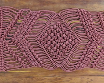 Pode incluir: Um corredor de mesa de macramé cor de vinho com um padrão geométrico e franjas nas pontas.