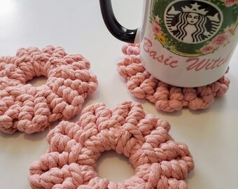 Pode incluir: Três  coasters de crochê rosa em forma de flor com uma caneca branca com alça preta e um design floral. A caneca diz "Basic Witch".