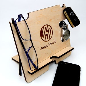 Puede incluir: Un soporte de tel&eacute;fono de madera con un monograma y un nombre personalizados, "JSD John Smith". Tiene ranuras para un tel&eacute;fono, gafas, reloj y llaves.