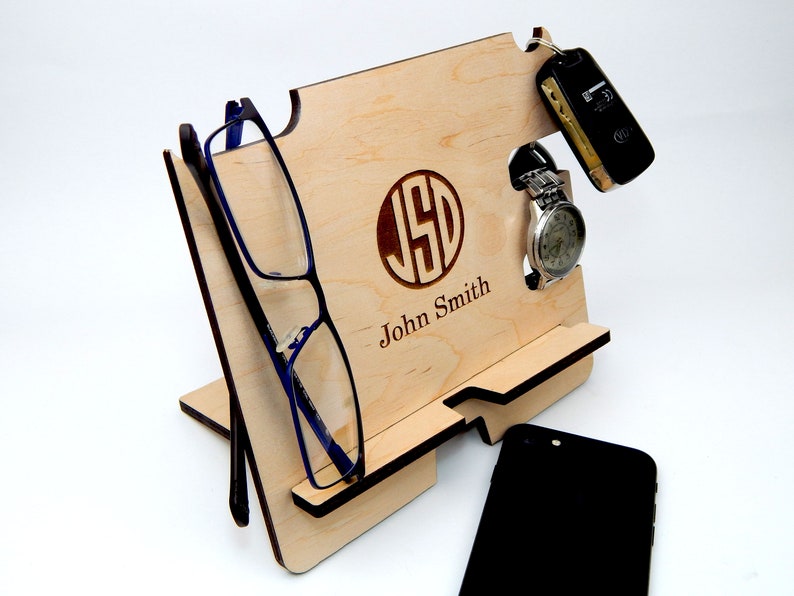 Puede incluir: Un soporte de tel&eacute;fono de madera con un monograma y un nombre personalizados, "JSD John Smith". Tiene ranuras para un tel&eacute;fono, gafas, reloj y llaves.