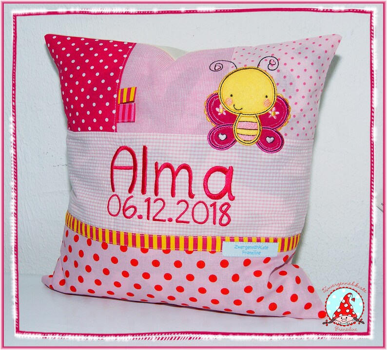 May include: Pink and yellow personalized pillow with a butterfly design and the name "Alma" and the date "06.12.2018" embroidered on it.