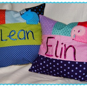 May include: Two colorful patchwork pillows with embroidered names "Lean" and "Elin" and appliqued animal designs. The pillow with the name "Lean" has a blue rhino, and the pillow with the name "Elin" has a pink elephant.