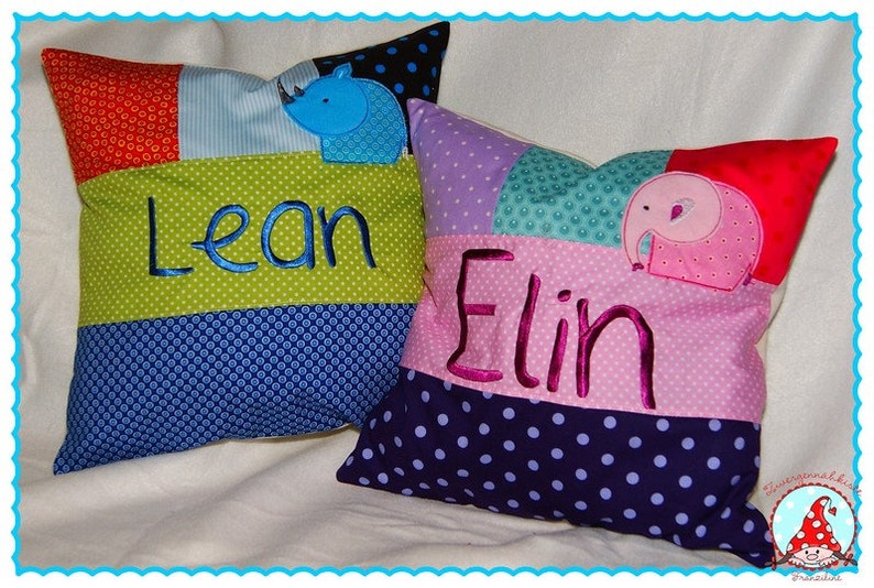 May include: Two colorful patchwork pillows with embroidered names "Lean" and "Elin" and appliqued animal designs. The pillow with the name "Lean" has a blue rhino, and the pillow with the name "Elin" has a pink elephant.