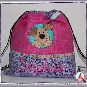 Könnte beinhalten: Rosaer Kordelzugbeutel mit einem niedlichen Cartoon-Hund und einem Marienkäfer, die auf der Vorderseite gestickt sind. Die Tasche hat einen lila-gepunkteten Boden mit dem Namen "Sophia", der in rosa gestickt ist.
