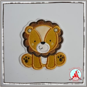 Könnte beinhalten: Eine gestickte Löwen-Applikation in Braun und Gelb auf weißem Hintergrund. Der Löwe hat eine braune Mähne, ein weißes Gesicht und einen lächelnden Mund. Der Löwe sitzt auf seinen Hinterbeinen mit ausgestreckten Pfoten.