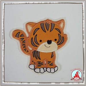 Könnte beinhalten: Ein orange-braunes gesticktes Bügelbild eines Cartoon-Tigers auf weißem Hintergrund. Der Tiger hat schwarze Streifen und ein weißes Gesicht mit schwarzen Augen und einem Lächeln.