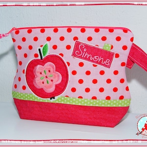May include: Pink polka dot bag with a red apple applique and the name "Simone" embroidered on a label. The bag features a red zipper, a green and white star trim, and a red strap. The bag is designed with a playful, whimsical aesthetic.