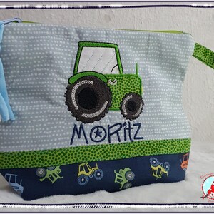 May include: A light blue zippered pouch with a green tractor applique and the name "MORITZ" embroidered in blue. The pouch has a green polka dot trim and a blue tractor pattern at the bottom. A blue tassel is attached to the side.