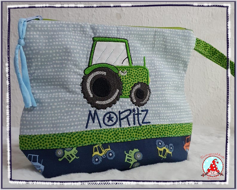May include: A light blue zippered pouch with a green tractor applique and the name "MORITZ" embroidered in blue. The pouch has a green polka dot trim and a blue tractor pattern at the bottom. A blue tassel is attached to the side.