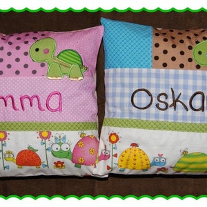 May include: Two colorful pillowcases with embroidered names "Emma" and "Oskar" and a turtle design. The pillowcases have a patchwork design with different colored fabrics and a border of small turtles and flowers.