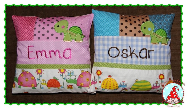 May include: Two colorful pillowcases with embroidered names "Emma" and "Oskar" and a turtle design. The pillowcases have a patchwork design with different colored fabrics and a border of small turtles and flowers.