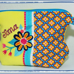 May include: A yellow cosmetic bag with a floral design and the name "Jana" embroidered on the front. The bag features a blue zipper, a handle, and a section with a repeating flower pattern in yellow, orange, and blue.