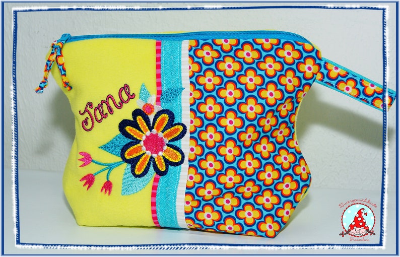 May include: A yellow cosmetic bag with a floral design and the name "Jana" embroidered on the front. The bag features a blue zipper, a handle, and a section with a repeating flower pattern in yellow, orange, and blue.