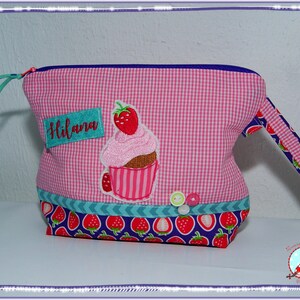 May include: Pink gingham fabric bag with a cupcake applique and the name "Hilana". The bag features a strawberry pattern on the bottom and handle, with a blue zipper and trim. Decorative buttons are sewn on the front.