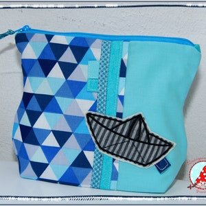 May include: A blue and white geometric pattern zippered pouch with a light blue body. A fabric applique of a paper boat is on the front. The pouch has a blue zipper and a blue fabric pull.