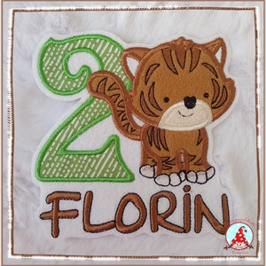 Könnte beinhalten: Grüne und braune Stickerei mit der Zahl 2, einem Tiger und dem Namen "FLORIN".