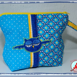 May include: A blue and white polka dot and floral patterned zippered pouch with a yellow zipper and handle. The pouch features an embroidered blue owl with closed eyes. The pouch is a handmade item.
