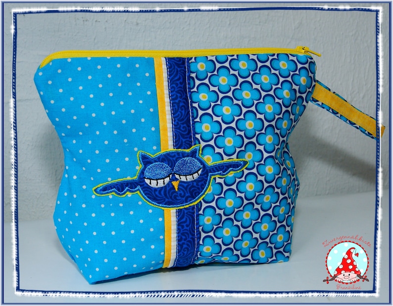 May include: A blue and white polka dot and floral patterned zippered pouch with a yellow zipper and handle. The pouch features an embroidered blue owl with closed eyes. The pouch is a handmade item.