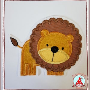Könnte beinhalten: Ein gestickter Löwenaufnäher mit goldgelbem Gesicht, einer dunkelbraunen, gewellten Mähne und einem kleinen Schwanz mit dunkelbrauner Spitze. Das Design zeigt eine schwarze Nase und Augen sowie einen weißen Rand um die Löwenform.