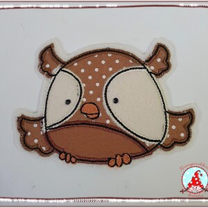 Könnte beinhalten: Eine braune Eulen-Applikation mit weißen Punkten und einem weißen Gesicht. Die Eule hat schwarze Augen und einen kleinen orangefarbenen Schnabel.