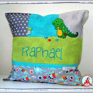 Könnte beinhalten: Ein grünes, blaues und graues Patchwork-Kissen mit einem Dinosaurier-Applique und dem Namen "Raphael" bestickt.