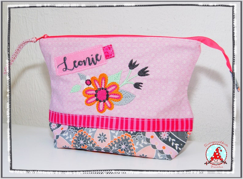 May include: Pink floral patterned zippered pouch with an embroidered flower design. The pouch has a pink zipper and a label that says "Leonic". The bottom of the pouch has a patterned fabric with gray, orange, and pink floral designs.