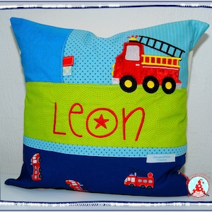 Könnte beinhalten: Ein grünes, blaues und rotes Kissen mit einem Feuerwehrauto-Design und dem Namen "Leon" darauf gestickt.