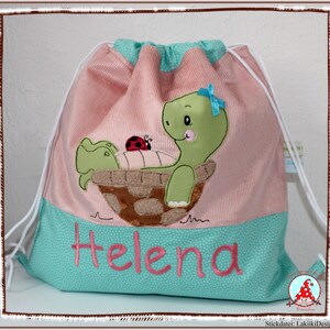 Könnte beinhalten: Eine rosa-türkise Kordelzugtasche mit einem grünen Schildkröten- und Marienkäfer-Motiv. Die Tasche hat den Namen "Helena" auf der Vorderseite gestickt.