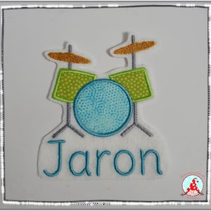 Könnte beinhalten: Ein personalisierter gestickter Aufnäher mit einem blauen, grünen und goldenen Schlagzeug und dem Namen "Jaron" in blauer Farbe.