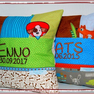 Könnte beinhalten: Zwei personalisierte Kissenbezüge mit gestickten Namen und Daten. Das erste Kissen hat ein braunes, blaues und grünes Patchwork-Design mit einem Hund, der hinter einem roten Hut hervorlugt. Das zweite Kissen hat ein braunes, blaues und graues Patchwork-Design mit einem Fuchs, der hinter einem grünen Blatt hervorlugt. Das erste Kissen sagt "Enno 30.09.2017" und das zweite Kissen sagt "Ats 06.2015".