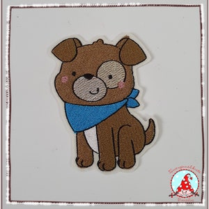 Könnte beinhalten: Ein brauner und weißer gestickter Cartoon-Hund, der ein blaues Bandana trägt. Der Hund sitzt mit gekreuzten Beinen und hat einen glücklichen Gesichtsausdruck.