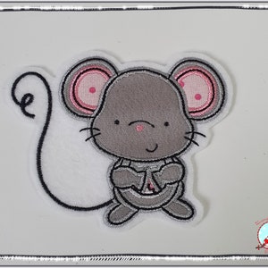 Könnte beinhalten: Eine graue gestickte Maus mit rosa Ohren und einem eingerollten Schwanz. Die Maus hält ihre Pfoten vor der Brust zusammen.