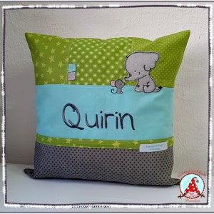 Könnte beinhalten: Ein grünes und graues Kissen mit einer blauen Tasche und dem Namen "Quirin" bestickt. Das Kissen zeigt eine Elefanten- und eine Maus-Applikation.