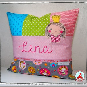 Könnte beinhalten: Ein rosa Kissen mit einem grünen, blauen und rosa Patchwork-Design. Das Kissen hat eine Prinzessin-Applikation mit einer Krone und den Namen "Lena" bestickt.