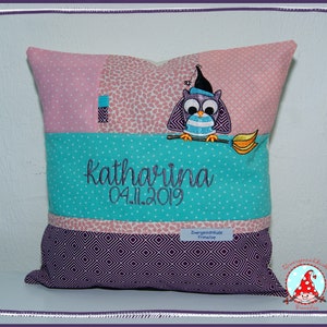 Könnte beinhalten: Ein rosa, türkisfarbenes und violettes Kissen mit einer weißen Eule, die einen schwarzen Hut trägt und einen Besen hält. Das Kissen hat den Namen "Katharina" und das Datum "04.11.2019" aufgestickt. Das Kissen hat auch ein kleines Etikett mit der Aufschrift "Zwergenstube Froschlein".