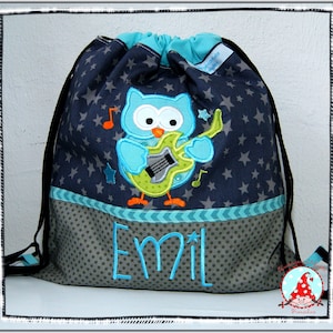 Könnte beinhalten: Eine blaue Kordeltasche mit grauem Hintergrund und weißen Sternen. Ein gestickter Eule mit einer Gitarre ist auf der Vorderseite der Tasche. Der Name "Emil" ist unten auf der Tasche gestickt.