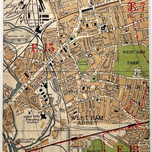 Puede incluir: Una impresión enmarcada de un mapa antiguo de la zona de West Ham, con calles, parques y puntos de referencia. El mapa está en tonos marrones y beige, con marcas y texto en rojo. La impresión está en un marco blanco.