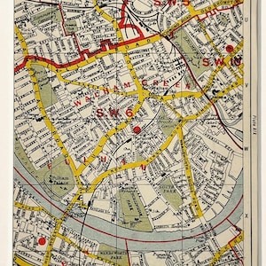 Op de afbeelding: Een ingelijste vintage kaart van Londen, met een gedetailleerde stratenkaart in geel en rood. De kaart bevat plaatsnamen zoals Hammersmith en South Park. De kaart is geplaatst tegen een witte achtergrond.