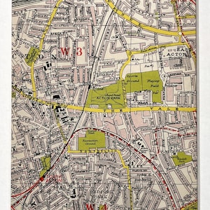 May include: Framed vintage map of Acton, London, showing detailed street layouts, parks, and landmarks. The map uses beige, green, and yellow, with red highlighting routes. The map is framed in a white mount and frame.