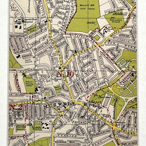 May include: A framed vintage map print featuring a detailed street map with green and yellow highlights. The map shows roads, parks, and buildings, with text labels. The print is set in a white mat and frame, suitable for home decor.