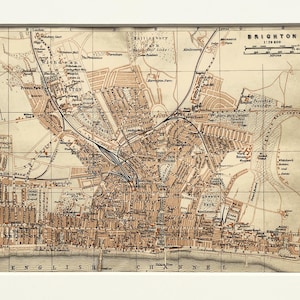 May include: A vintage-style map of Brighton, England, printed in black and tan ink on paper. The map features a grid system, street names, railway lines, and a scale bar. It is presented inside a white rectangular mat board frame.