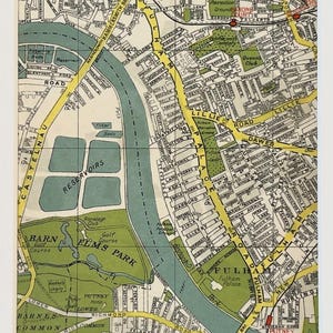 Op de afbeelding: Een ingelijste vintage kaartafdruk met een gedetailleerde stratenkaart van een Londense wijk. De kaart gebruikt gele, groene en blauwe tinten, met leesbare straatnamen en herkenningspunten. De afdruk wordt gepresenteerd in een witte lijst.