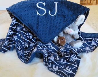 Puede incluir: Una manta para bebé azul marino y blanca con un patrón de flechas blancas. La manta está doblada y tiene una textura suave. La manta está bordada con las iniciales "SJ".