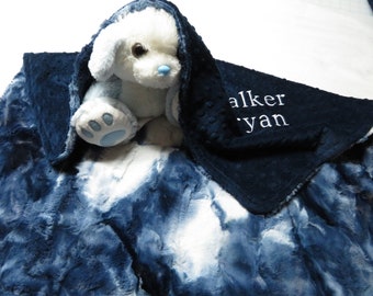 May include: A blue and white faux fur baby blanket with a blue minky backing. The blanket has a white plush toy dog peeking out from under it. The blanket is personalized with the name "Walker Ryan" in white embroidery.