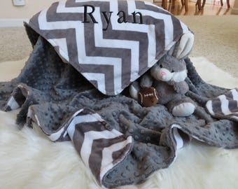 May include: A gray and white chevron patterned baby blanket with a gray plush minky backing. The blanket has the name "Ryan" embroidered on it. A gray plush bunny toy is sitting on the blanket, holding a football.