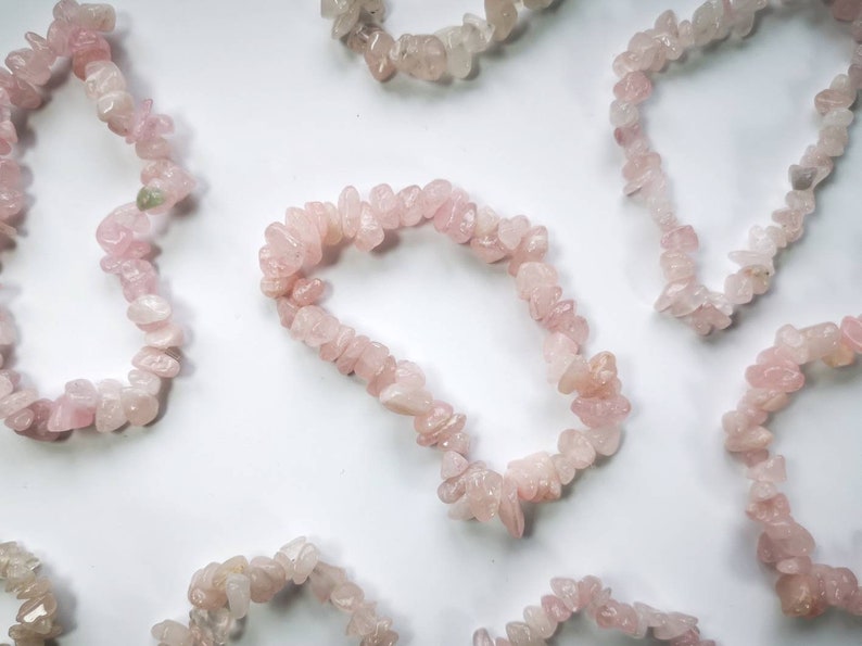 May include: A collection of six pink rose quartz chip bracelets. Each bracelet is made of small, irregular shaped chips of rose quartz, strung together on a clear elastic cord.