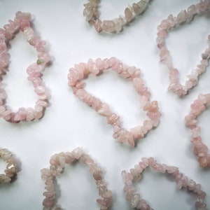 May include: A collection of pink rose quartz chip bracelets. The bracelets are made of small, irregular pieces of rose quartz that are strung together on elastic.